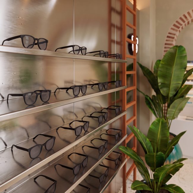 Detalle de gafas en exhibidor metálico junto a vegetación tropical